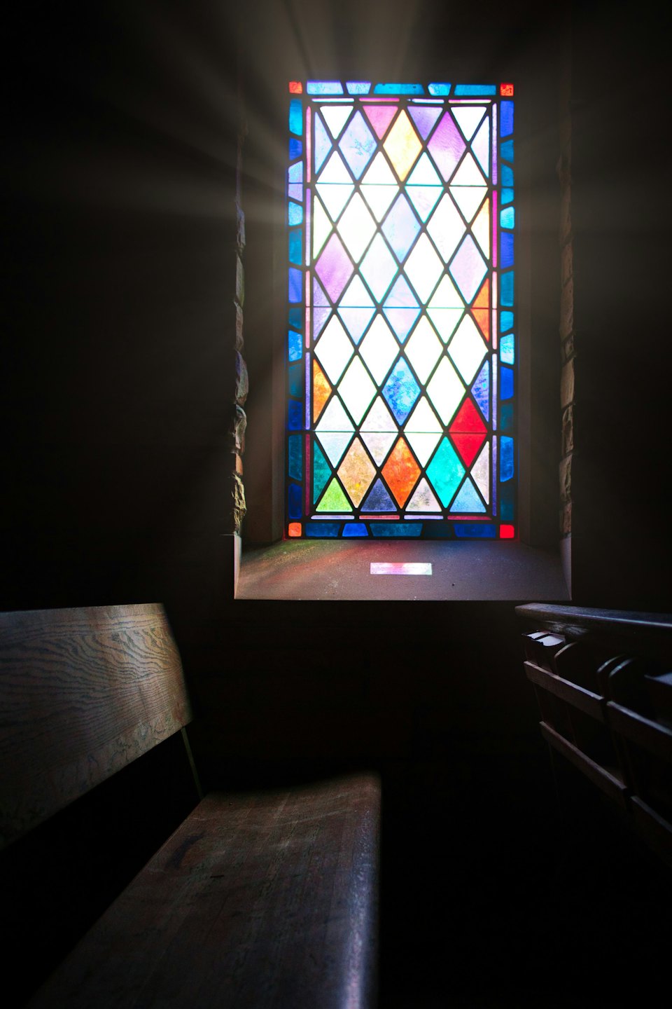 Sunlight streams through a colorful stained glass window onto a pew.