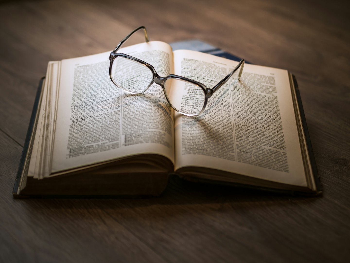 Antique book with reading glasses on a wooden table.