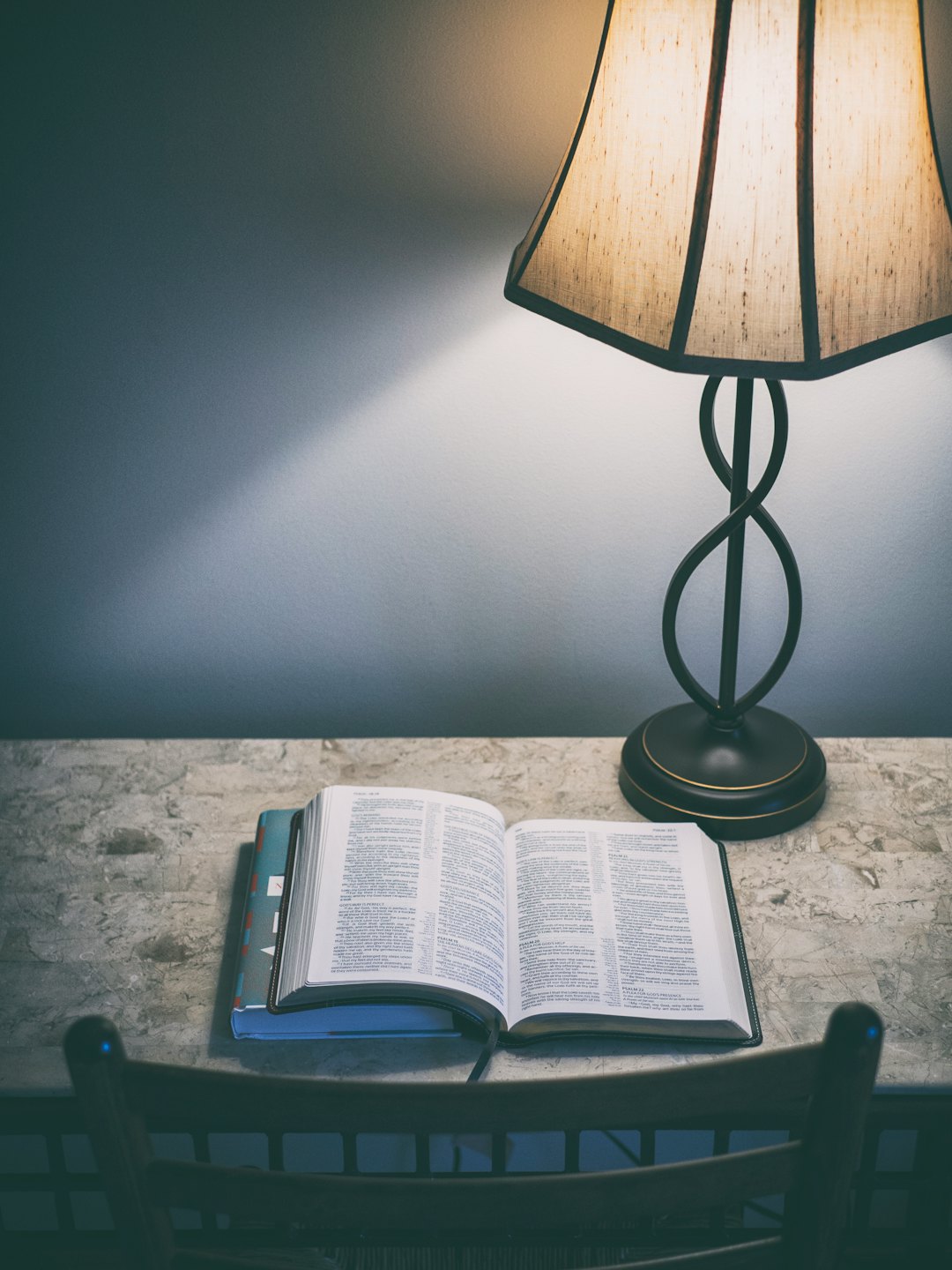 An open Bible rests on stacked books beside a lamp.